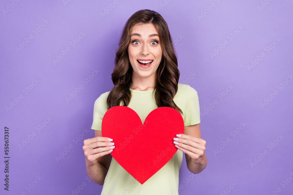 Photo of funny young lady wear t-shirt impressed shocked her present valentine day hold red love symbol isolated on purple color background Photo of funny young lady wear t-shirt impressed shocked her present valentine day hold red love symbol isolated on purple color background