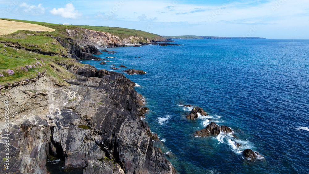 Fototapeta premium Farm fields on the rocky shore of the Celtic Sea, south of Ireland, County Cork. Beautiful coastal area. Turquoise waters of the Atlantic. Picturesque stone hills. Aerial photo. Drone point of view.
