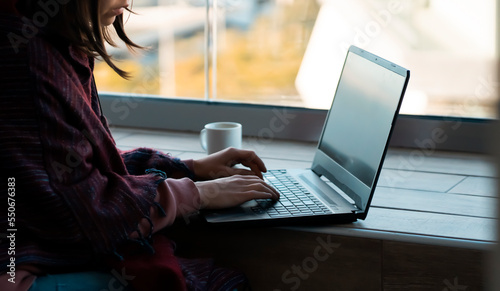 Girl is working at a laptop, typing on a keyboard indoors.