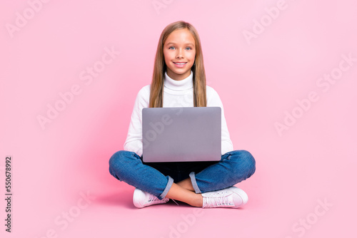 Full size portrait of positive smart schoolchild sit floor use wireless netbook isolated on pink color background © deagreez