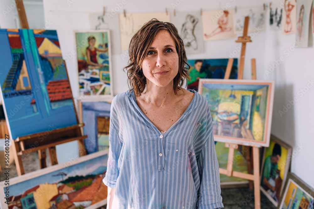 Female artist standing in art studio with various paintings Female artist standing in art studio with various paintings