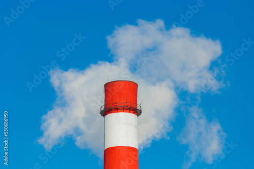 Pollution of the environment, ecology and air. Withdrawal of combustion products of soot, smoke and gases from the pipe of an industrial plant into the atmosphere against the background of a blue sky