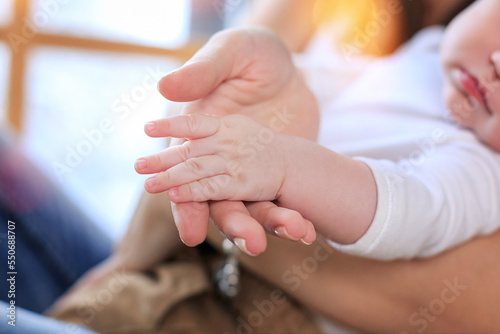 Close up young mother hold hand of small tiny cute baby son daughter. Mom holding innocent child in arms, hugging kid with love, care, affection. Growth, infant health care, happy motherhood concept. photo