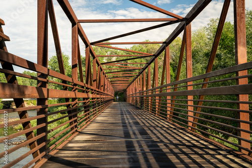 Fototapet bike trail and a long footbridge over a river with distant cyclist - Poudre Rive