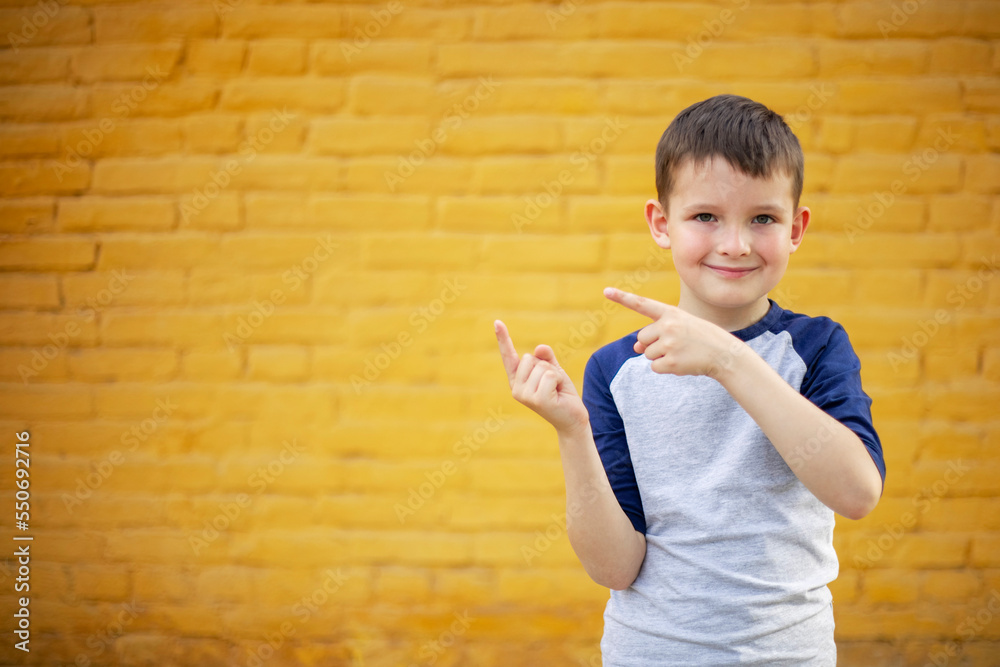 Smiling cute kid pointing with finger aside on yellow brick wall background Smiling cute kid pointing with finger aside on yellow brick wall background