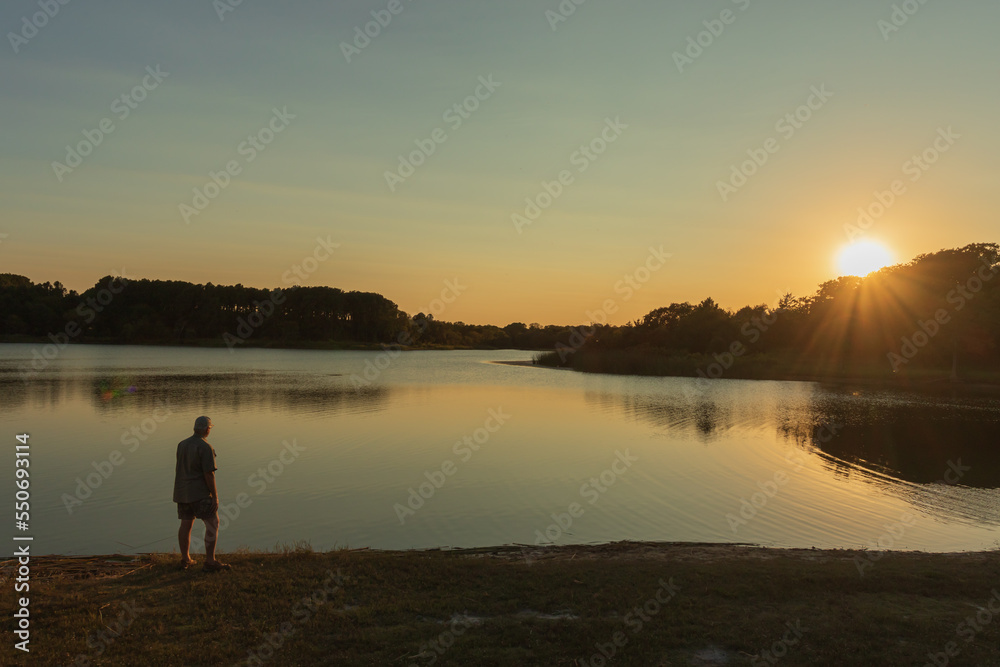 Senior man standing next to a lake watching the sun go down. Senior man standing next to a lake watching the sun go down.