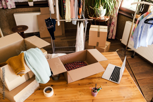 High angle view of desk with cardboard box parcel with clothes, clothes resale concept.