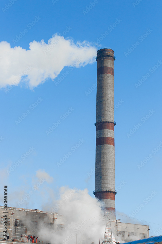 Pollution of the environment, ecology and air. Withdrawal of combustion products of soot, smoke and gases from the pipe of an industrial plant into the atmosphere against the background of a blue sky Pollution of the environment, ecology and air. Withdrawal of combustion products of soot, smoke and gases from the pipe of an industrial plant into the atmosphere against the background of a blue sky