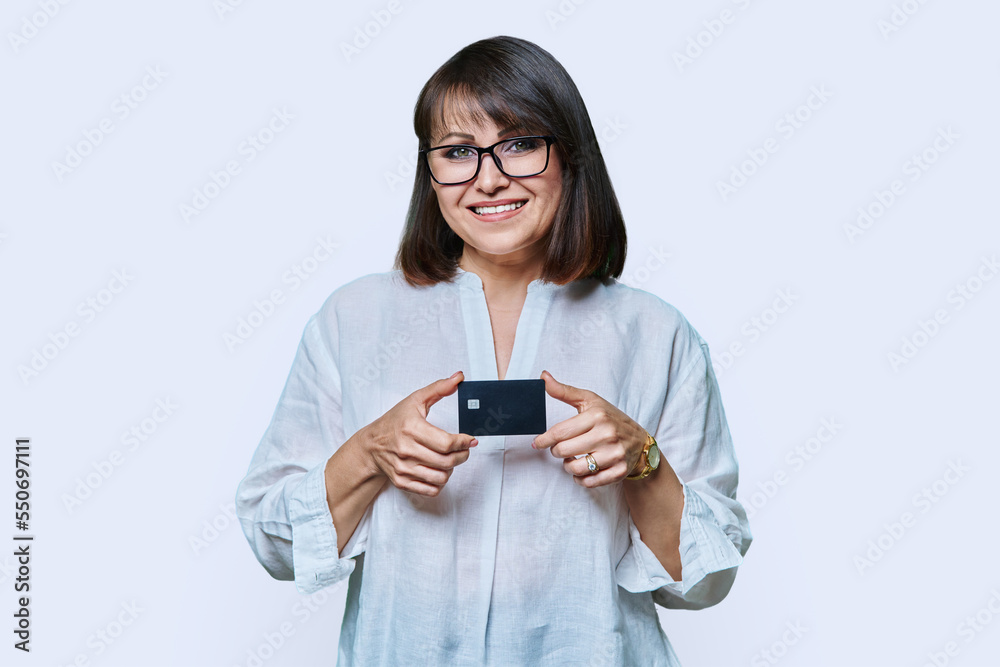 Attractive middle aged smiling woman holding plastic credit card, white background Attractive middle aged smiling woman holding plastic credit card, white background