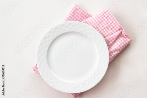 Empty white plate with pink fabric napkin, a fork and a knife on white table. Top view.