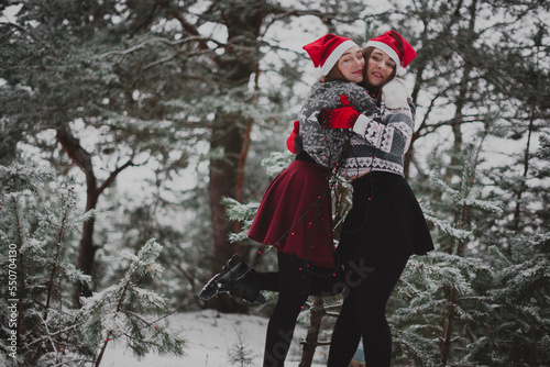 Two young teenage hipster girl friends together.Close up fashion portrait of two sisters hugs and having fun winter time,wearing red santa hats and sweater,best friends couple outdoors, snowy weather