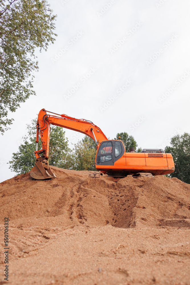 orange tractor or excavator with a bucket on the sand. a large working machine for laying sewers and communal communications. construction of roads and houses, water supply. engineering and orange tractor or excavator with a bucket on the sand. a large working machine for laying sewers and communal communications. construction of roads and houses, water supply. engineering and