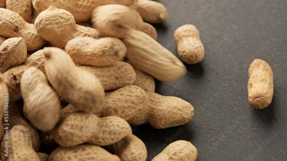 Peanuts in shell falling on black table. Organic food. Pile of roasted