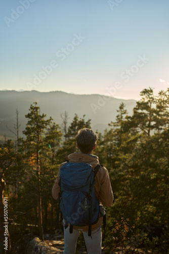 Rear view hiker man with backpack enjoying sunset and mountains, hiking expedition outdoors, travel destination