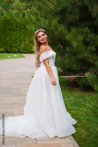 a blonde bride on a path in the park in a white long dress.