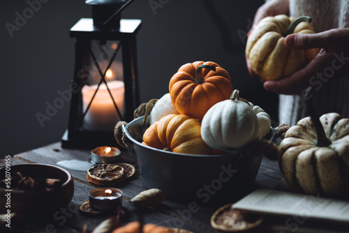 Autumn home composition with aromatic candles. Woman in wool sweater holding a pumpkin. Aromatherapy on a grey fall morning, atmosphere of cosiness and relax. Wooden dark background