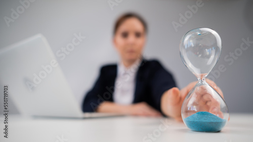 Business woman flipping an hourglass at her desk. 