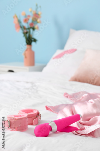 Pink vibrator and handcuffs on white bed, closeup