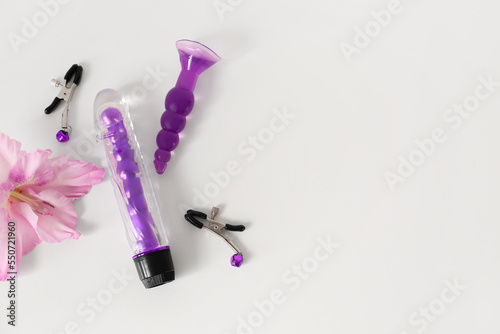 Purple sex toys with flower on white table, top view