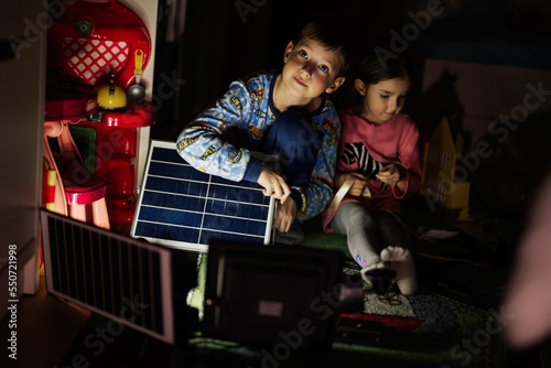 Children playing at home during a blackout using alternative lighting with solar panel.