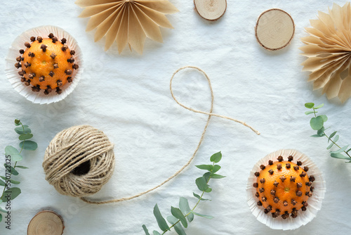 Fragrant pomander balls handmade from tangerines with cloves. Handmade paper stars from brown baking paper. Flat lay on off white textile with eucalyptus. Wood circles, hemp cord.