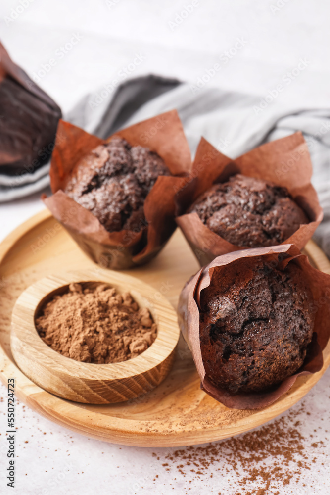 Wooden plate with tasty chocolate muffins and cocoa powder on light background, closeup Wooden plate with tasty chocolate muffins and cocoa powder on light background, closeup