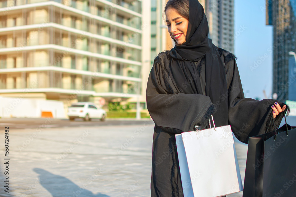 Young muslim woman enjoying shopping time in the city of Abu Dhabi. Beautiful Arabic woman with shopping bags on the street.
