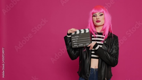 Glamour carefree woman holding film slate and saying action, preparing to record video montage or footage. Young beautiful person with filming equipment, filmmaker over background. photo