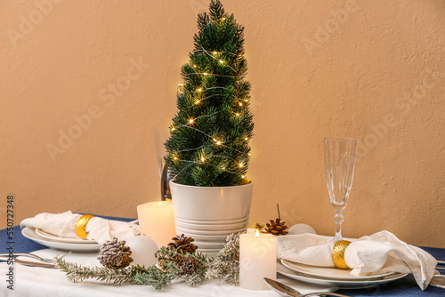 Table setting with small Christmas tree, fir cones and candles near beige wall