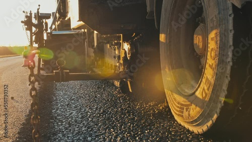 Close up of fresh asphalt and asphalt paver wheels. The rays of the setting sun. Road repair. Road construction machines. Work on the road.