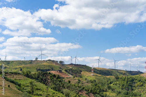 The wind turbines in the top of the grass hill underneath the group of white clouds and blue sky on a sunny day, produced electricity from pure energy. © Surachetsh