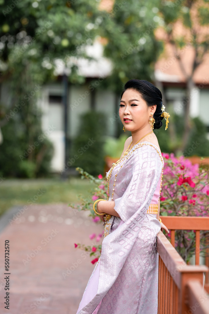 A woman in a traditional Thai costumes is standing on the wooden bridge while being taken a portrait photo shooting. A woman in a traditional Thai costumes is standing on the wooden bridge while being taken a portrait photo shooting.
