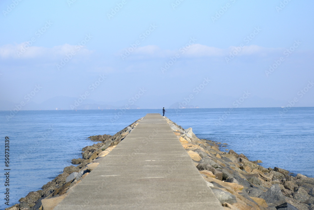 People fishing at the end of a breakwater on a clear blue sky day in the Seto Inland Sea.