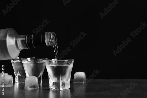 Pouring vodka from bottle in glass and ice cubes on grey table. Space for text