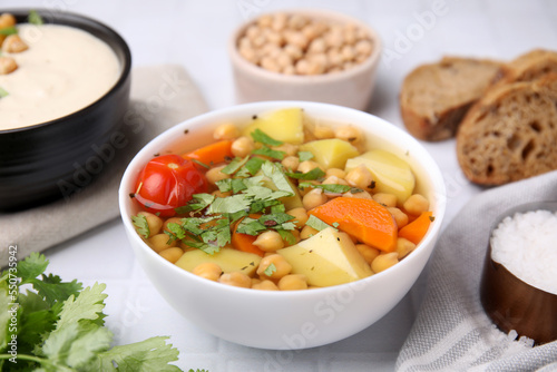 Tasty chickpea soup in bowls on white tiled table, closeup