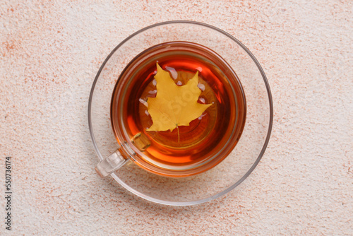 Cup of tasty tea and autumn yellow leaf on color background, top view