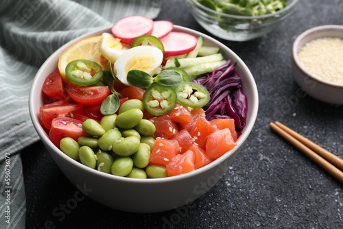 Poke bowl with salmon, edamame beans and vegetables on black table