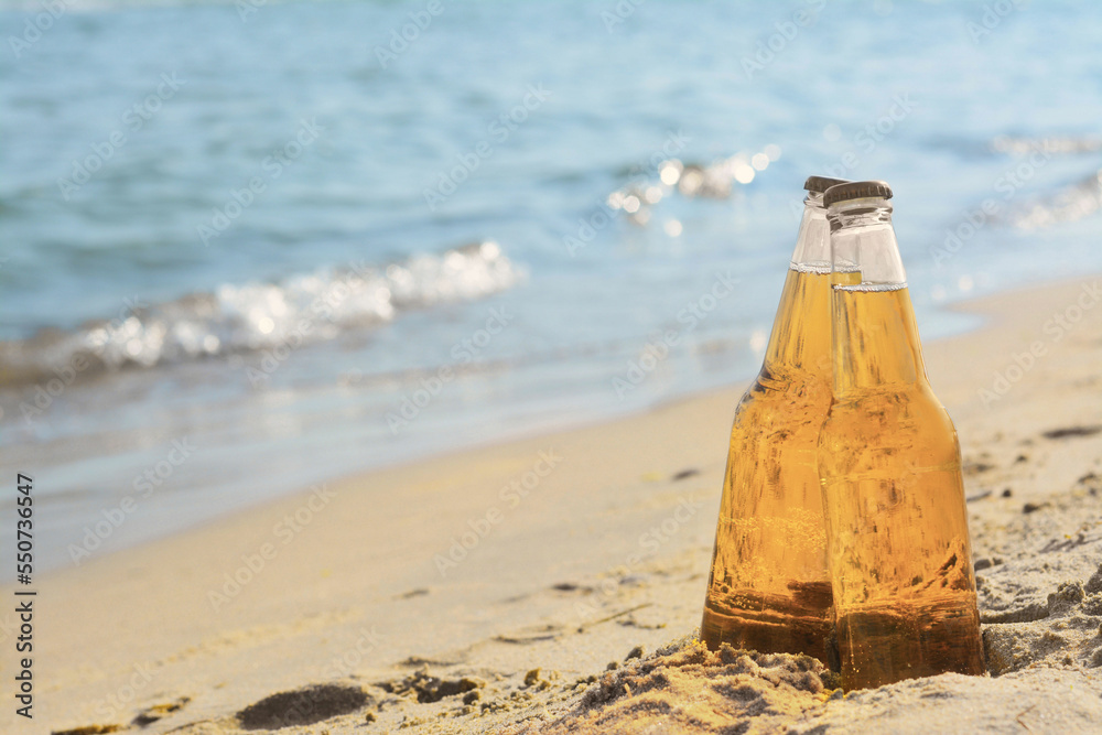 Bottles of cold beer on sandy beach near sea, space for text Bottles of cold beer on sandy beach near sea, space for text