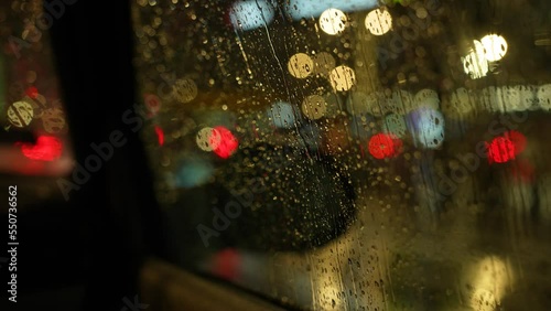 Driving on the rainy night. View through the car window on a rainy night. Raindrops run down the car window. 