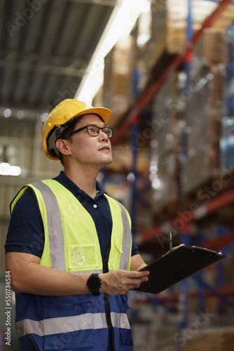 Vertical Portrait of Asian man warehouse supervisor working distribution warehouse to and managing inventory and logistics. Industrial inspector working in factory place.