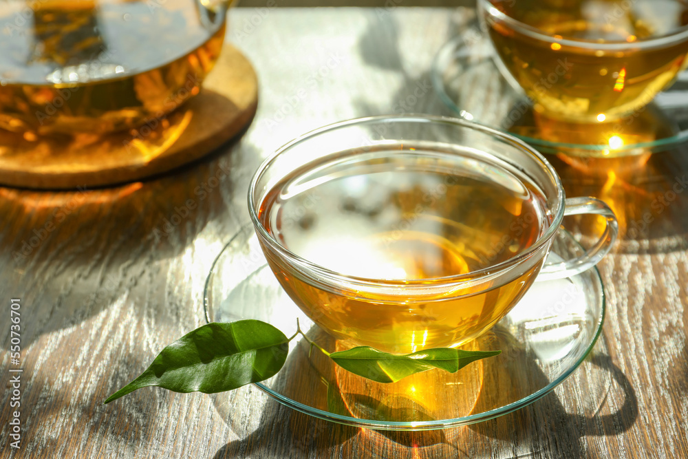 Fresh green tea in glass cups with saucers and leaves on wooden table Fresh green tea in glass cups with saucers and leaves on wooden table