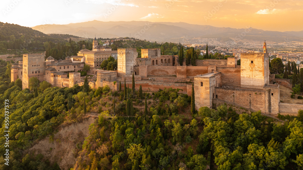 Sunrise aerial photo of the Alhambra fortress in Granada, Spain. The fortress is bathed in golden light.