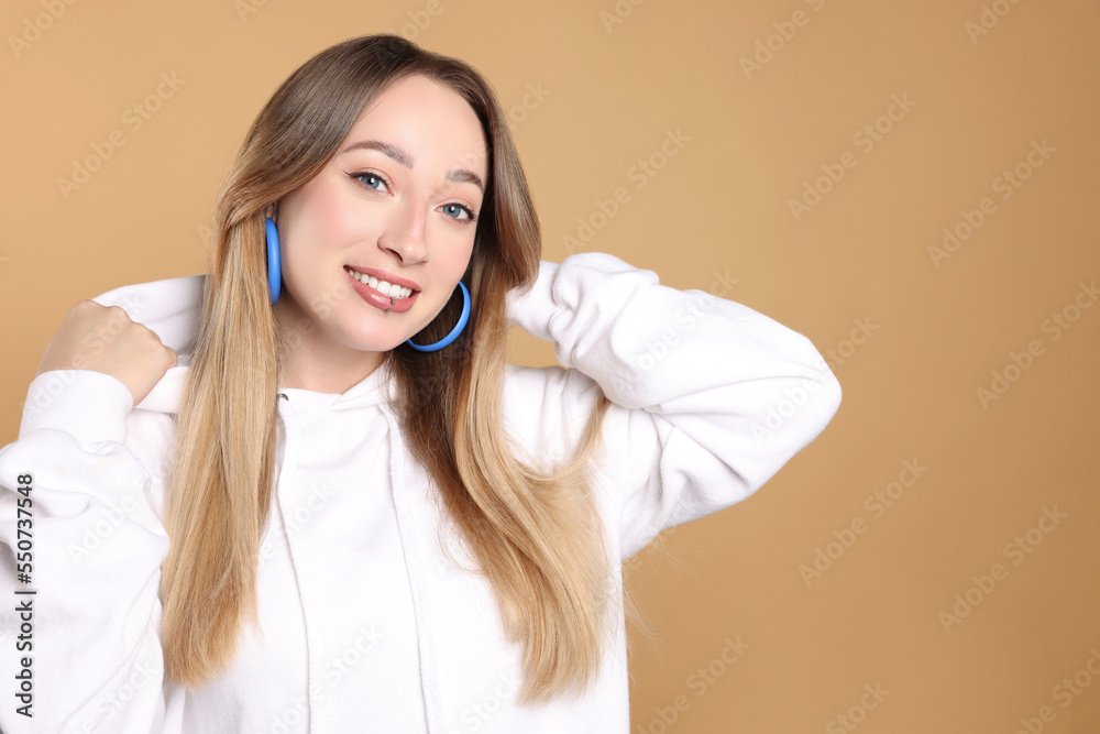 Young woman with lip piercing on beige background