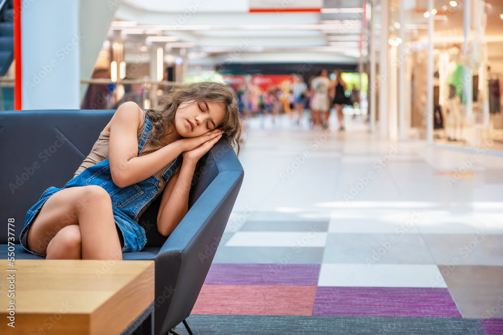 Tired teenage girl sleeping on sofa in shopping mall