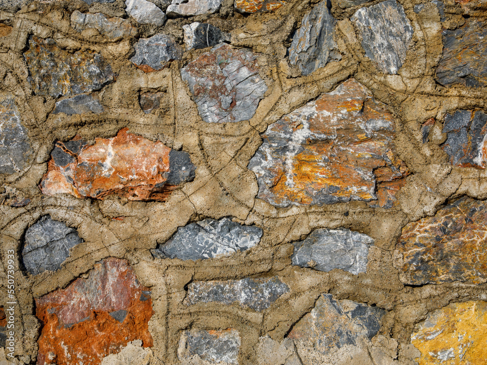 Fototapeta premium Old stone wall close up in orange beige blue grey palette. Stone tile with cement joints background with detailed natural texture. Historical building facade.