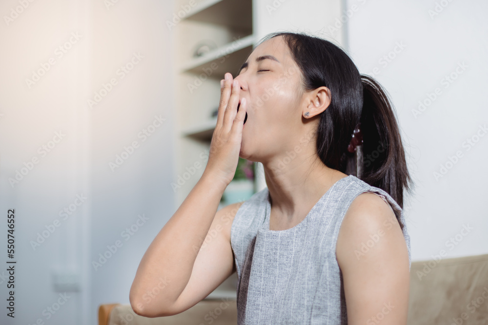 Asian woman yawning while working on laptop in her office. Asian woman yawning while working on laptop in her office.