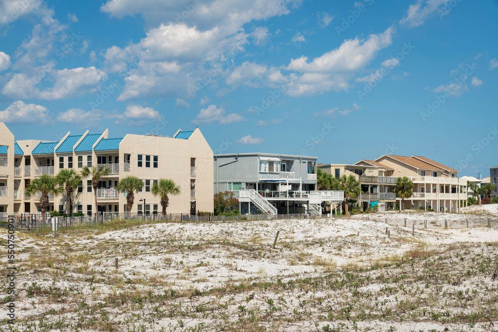 Grasses on a white sand dunes near the fenced residential buildings against the sky in Destin, FL Grasses on a white sand dunes near the fenced residential buildings against the sky in Destin, FL