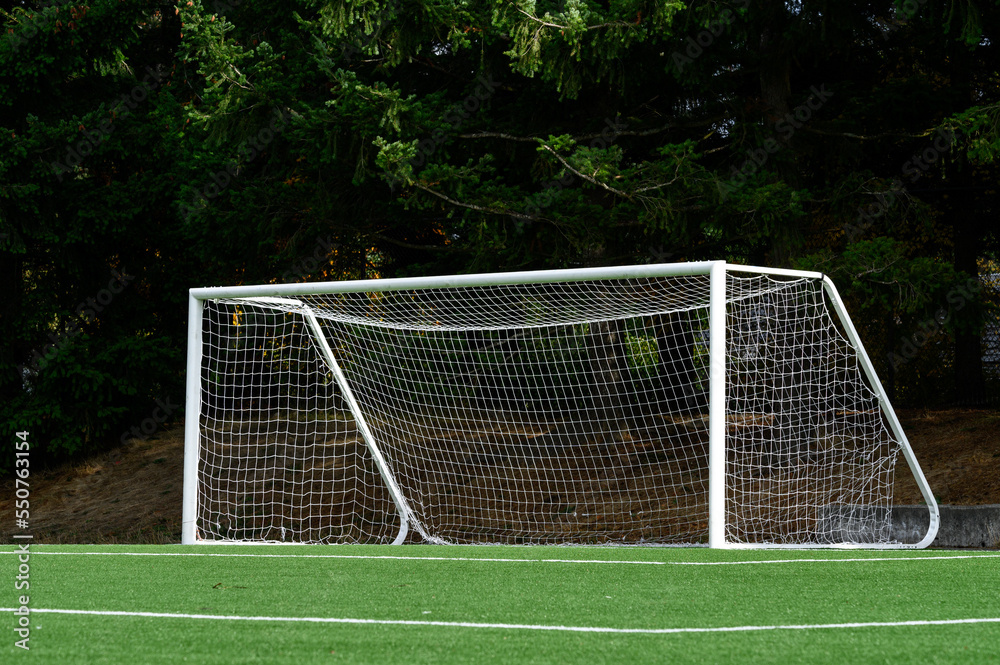 Empty soccer goal with white net on a sunny day, artificial turf field

