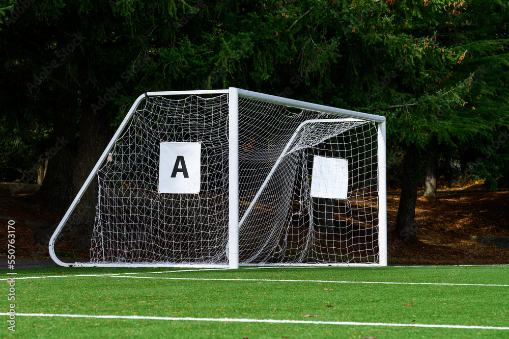 Fototapeta premium Empty soccer goal with white net on a sunny day, artificial turf field 