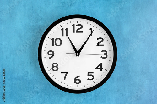 Modern analog clock, round in black and white, on a blue background 